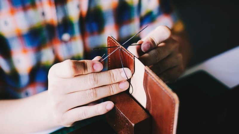 person knitting a leather wallet